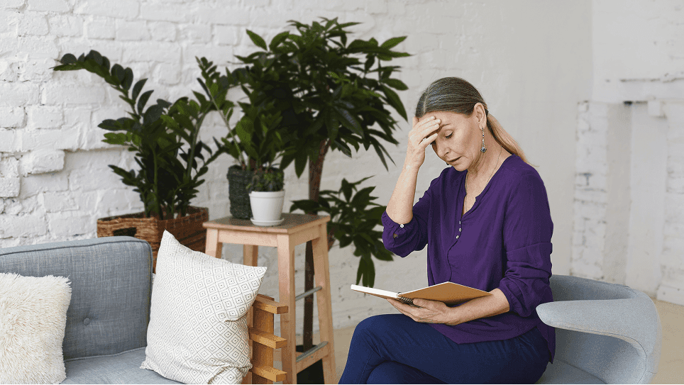 Woman holding her forehead while reading at home