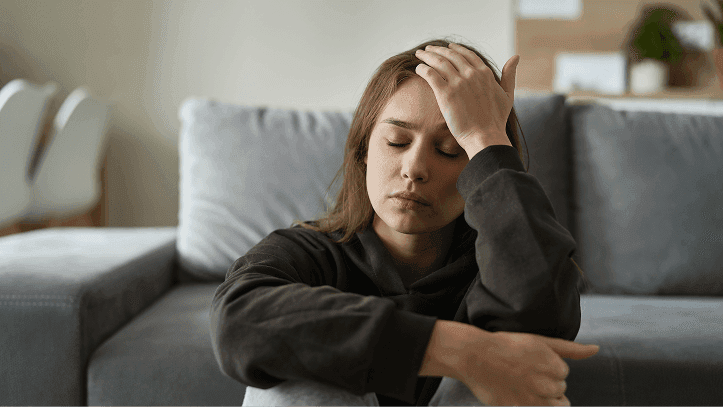 Woman sitting on a couch holding her head, feeling anxious