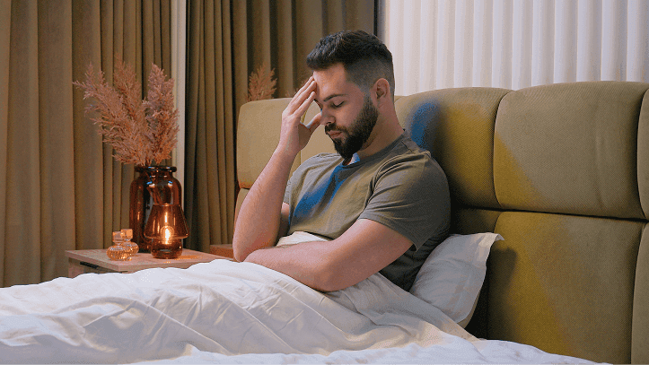 Man sitting up in bed holding his forehead