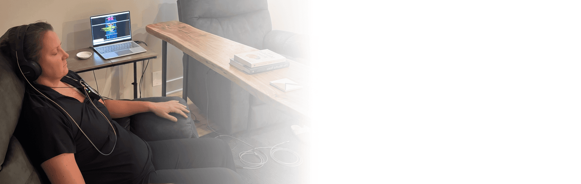 Client relaxing in a recliner with a neurofeedback headset beside a laptop