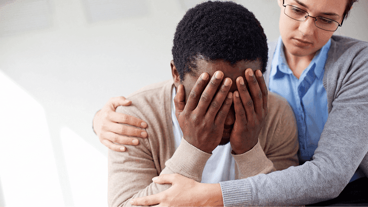 Man covering his face while a caregiver comforts him
